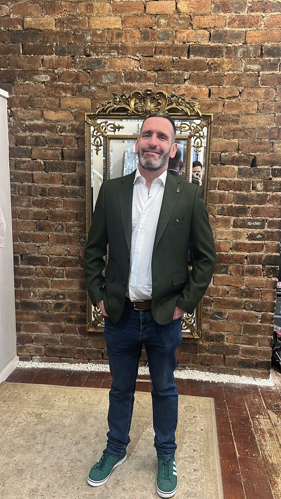 Customer wearing a green blazer with jeans and green trainers.