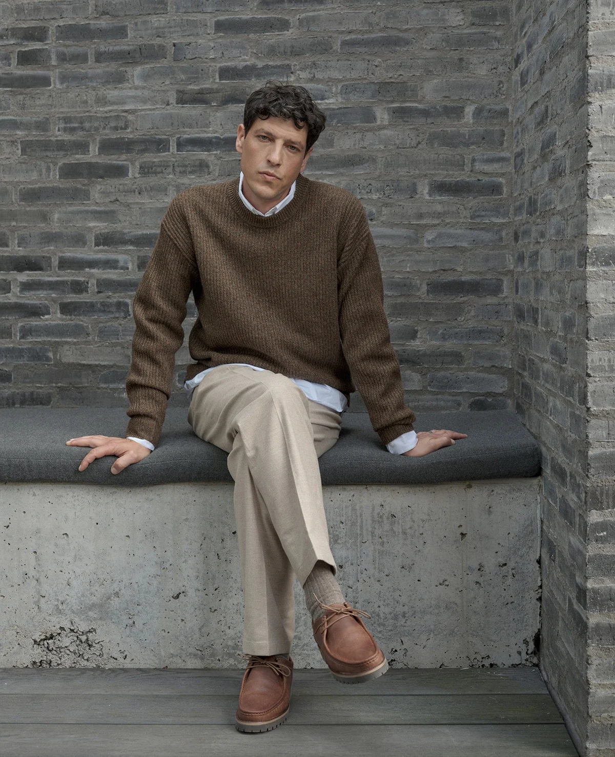 Brown knitwear layered over a pale shirt with light trousers