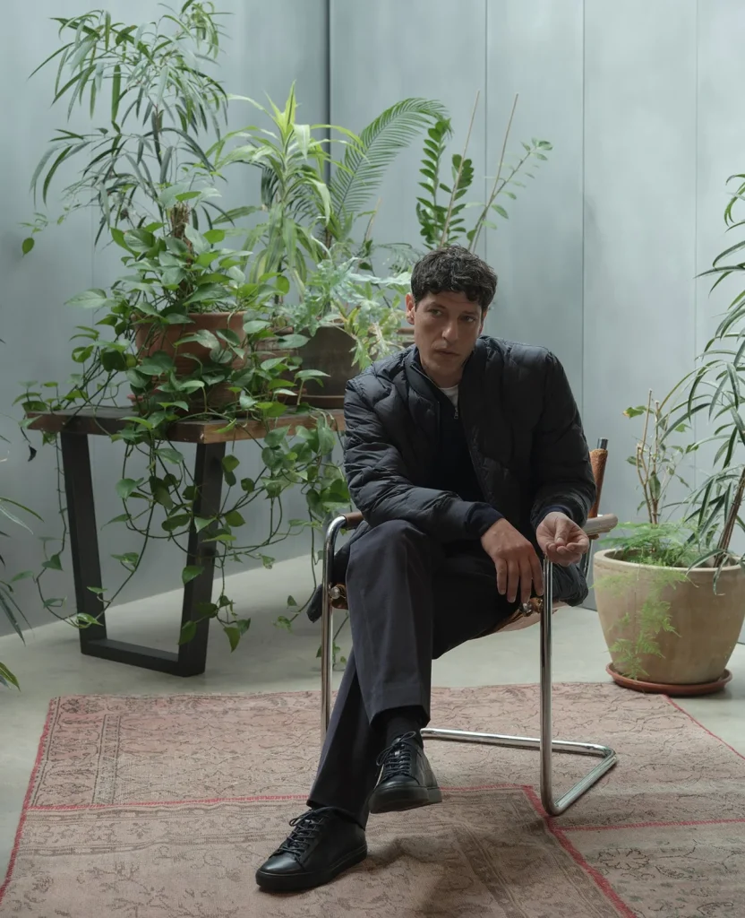 Model wearing a black jacket seated beside plants