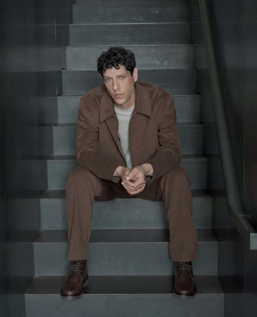 Model wearing a brown jacket and grey knit seated on stairs